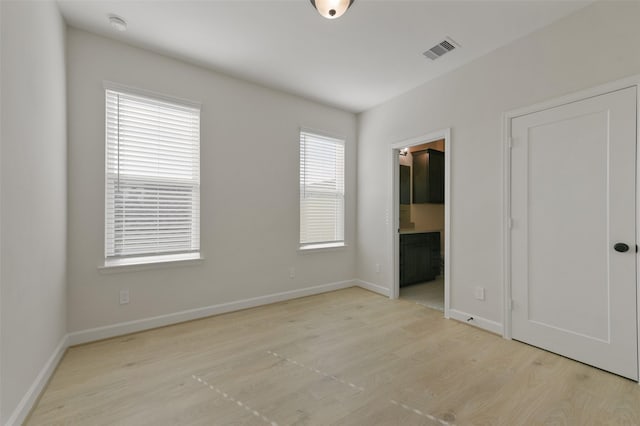 unfurnished bedroom with light hardwood / wood-style flooring, connected bathroom, and multiple windows