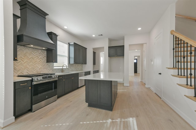 kitchen with a center island, light hardwood / wood-style flooring, premium range hood, backsplash, and appliances with stainless steel finishes