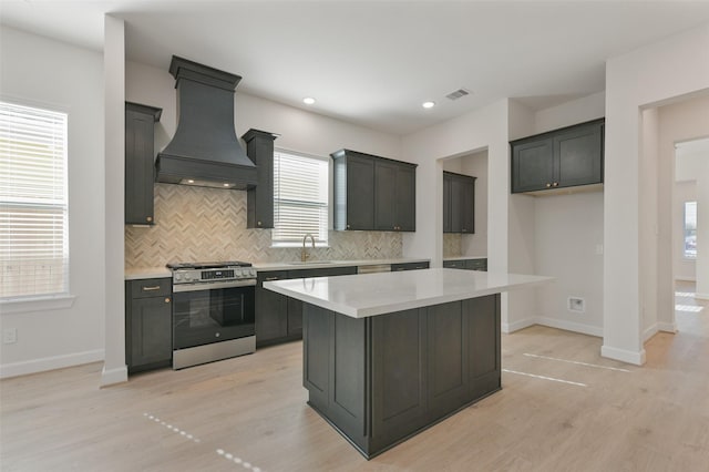 kitchen with custom exhaust hood, a center island, a healthy amount of sunlight, and gas range