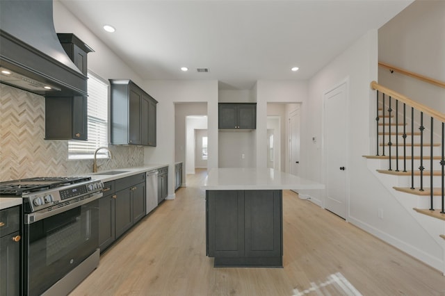 kitchen with sink, a center island, light wood-type flooring, appliances with stainless steel finishes, and custom exhaust hood