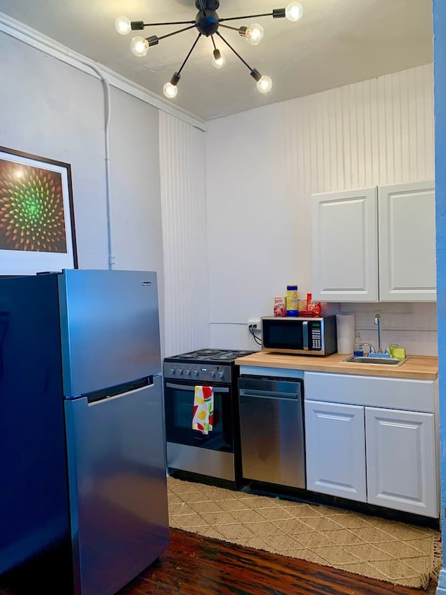 kitchen with appliances with stainless steel finishes, white cabinetry, sink, crown molding, and dark wood-type flooring