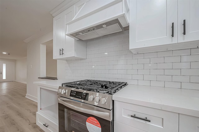 kitchen with stainless steel gas range, custom exhaust hood, light countertops, tasteful backsplash, and white cabinetry