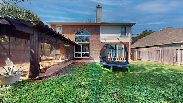 rear view of house with a sunroom, a lawn, and a trampoline