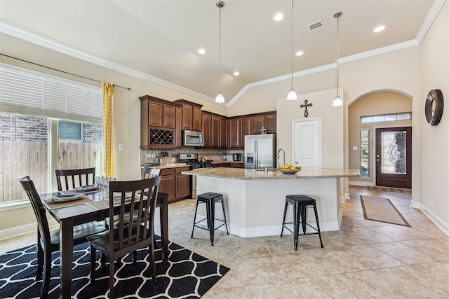 kitchen with decorative backsplash, vaulted ceiling, a kitchen island with sink, stainless steel appliances, and light stone counters