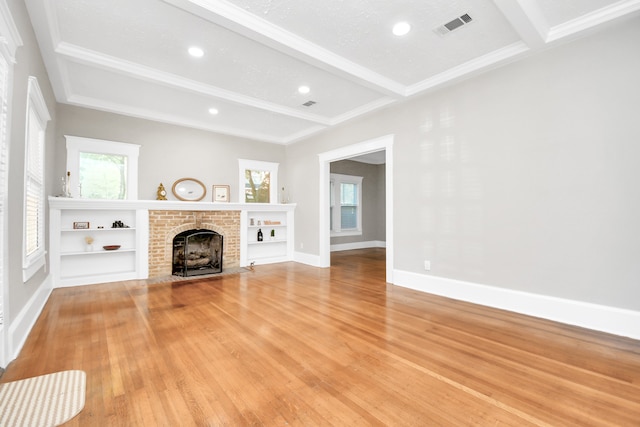 unfurnished living room with beam ceiling, light wood-type flooring, a textured ceiling, and a brick fireplace