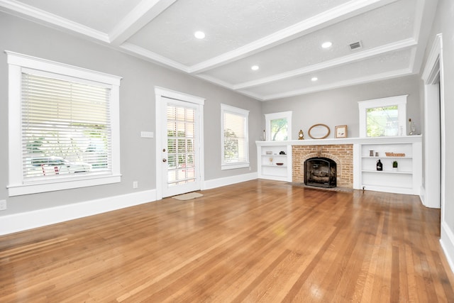 unfurnished living room with hardwood / wood-style floors, a wealth of natural light, beamed ceiling, and a brick fireplace