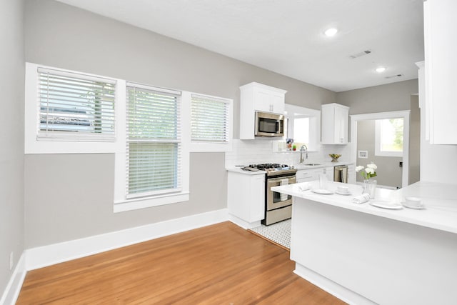 kitchen with white cabinetry, sink, hardwood / wood-style floors, decorative backsplash, and appliances with stainless steel finishes