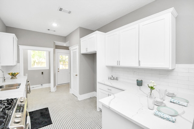 kitchen featuring white cabinetry, stainless steel range, sink, tasteful backsplash, and light stone counters