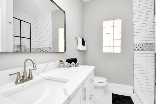 bathroom with a tile shower, vanity, toilet, and tile patterned floors