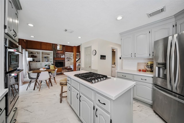 kitchen featuring stainless steel appliances, white cabinetry, a breakfast bar, a textured ceiling, and a kitchen island