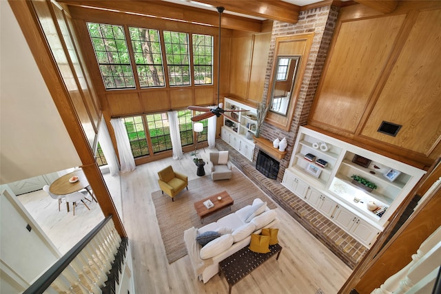 living room featuring wood walls, ceiling fan, light hardwood / wood-style floors, and beam ceiling