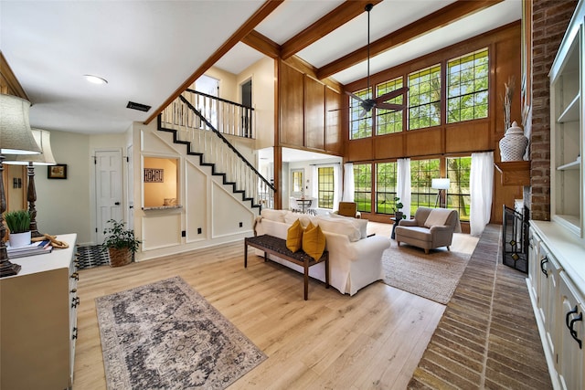 living room with a brick fireplace, light wood-type flooring, a high ceiling, and beam ceiling