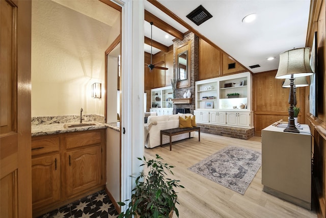 living room with sink, ceiling fan, beam ceiling, wooden walls, and light wood-type flooring