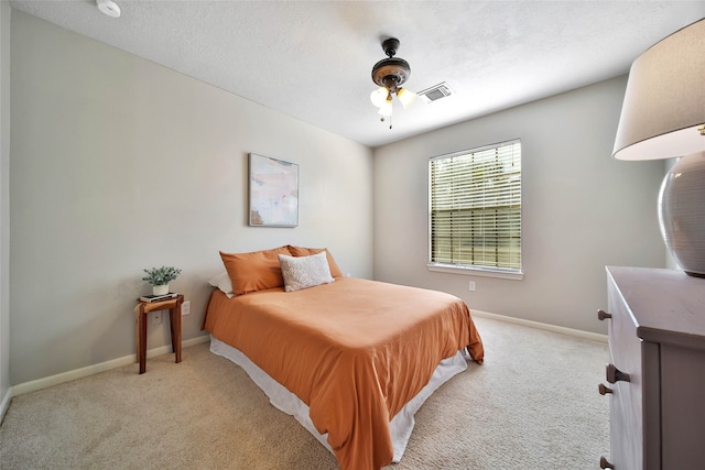 bedroom featuring a textured ceiling, light colored carpet, and ceiling fan