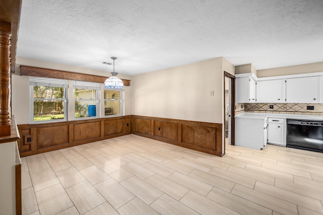 kitchen with dishwasher, wood walls, backsplash, hanging light fixtures, and white cabinetry