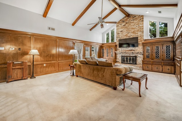 carpeted living room featuring beam ceiling, ceiling fan, a brick fireplace, high vaulted ceiling, and wood walls