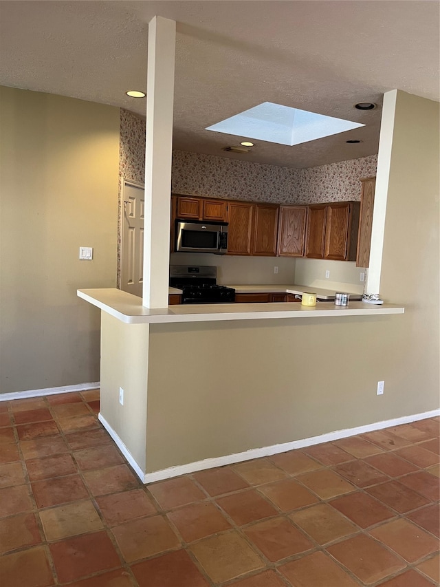 kitchen featuring kitchen peninsula, black range with gas stovetop, a skylight, and tile patterned flooring