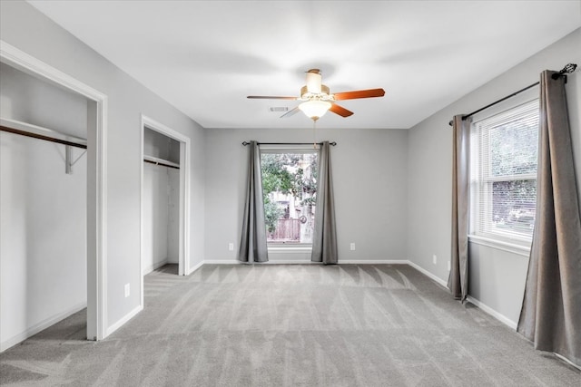 unfurnished bedroom with light colored carpet, multiple windows, ceiling fan, and two closets