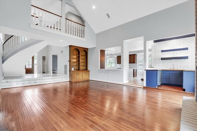 unfurnished living room featuring hardwood / wood-style flooring, high vaulted ceiling, a healthy amount of sunlight, and sink