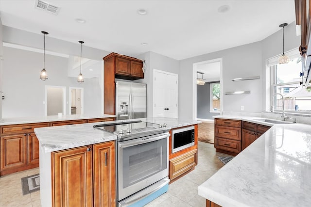 kitchen featuring stainless steel appliances, hanging light fixtures, a kitchen island, and light stone counters