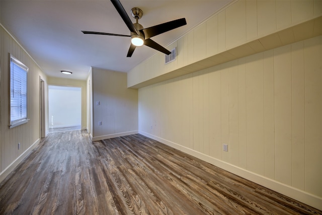 empty room featuring dark wood-type flooring, wooden walls, and ceiling fan