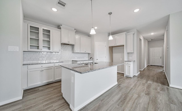 kitchen with visible vents, glass insert cabinets, light stone countertops, white cabinetry, and a sink