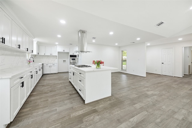 kitchen with island range hood, stainless steel gas cooktop, white cabinets, a center island, and light hardwood / wood-style floors