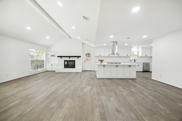 unfurnished living room with light wood-type flooring, vaulted ceiling with beams, a fireplace, and sink