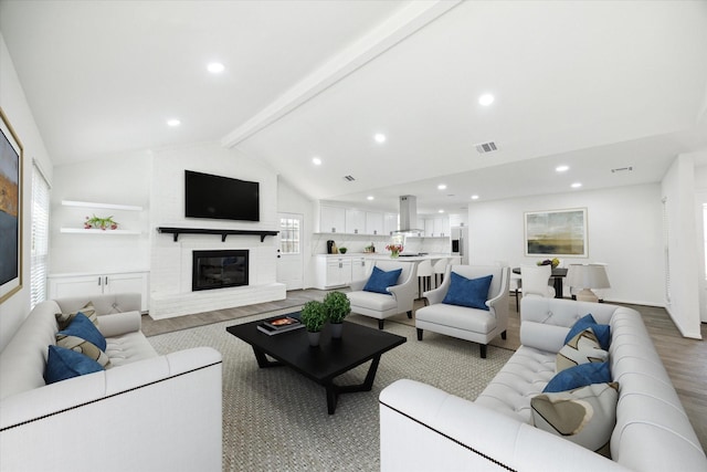 living room featuring a brick fireplace, lofted ceiling with beams, and light hardwood / wood-style floors