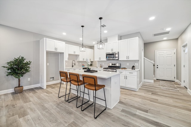 kitchen with light hardwood / wood-style flooring, a kitchen island, hanging light fixtures, and stainless steel appliances