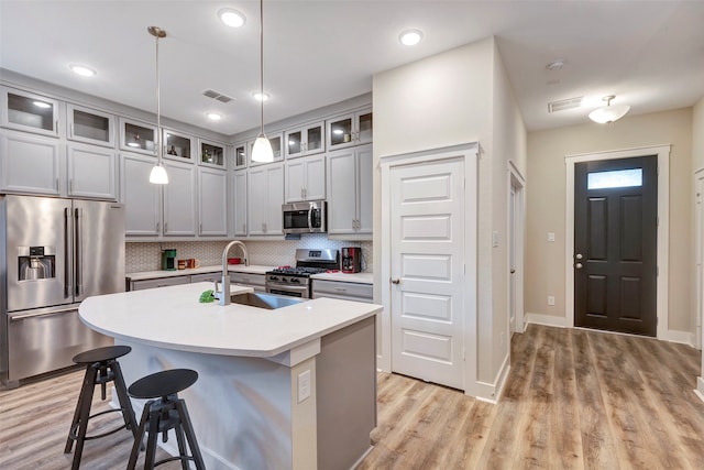 kitchen with appliances with stainless steel finishes, tasteful backsplash, sink, pendant lighting, and an island with sink