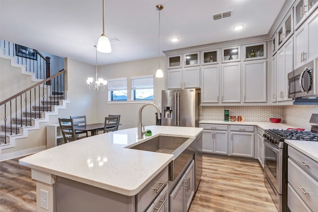 kitchen featuring appliances with stainless steel finishes, a center island with sink, hanging light fixtures, and light hardwood / wood-style floors