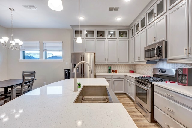 kitchen featuring light stone countertops, pendant lighting, stainless steel appliances, and sink