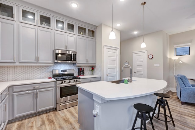 kitchen with pendant lighting, a kitchen island with sink, light hardwood / wood-style flooring, decorative backsplash, and stainless steel appliances