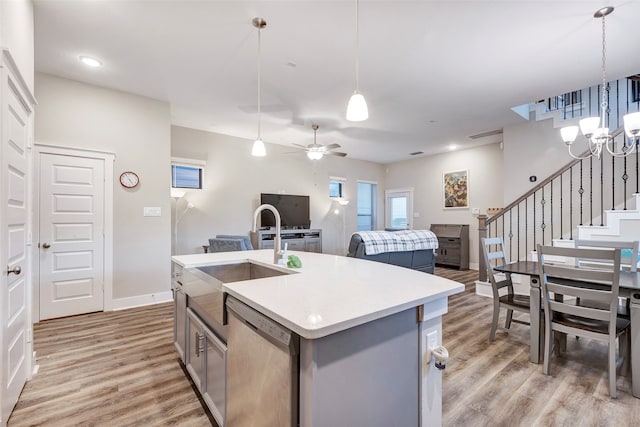 kitchen featuring light wood-type flooring, sink, dishwasher, hanging light fixtures, and an island with sink