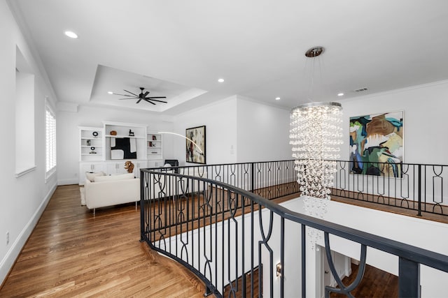 hall featuring a tray ceiling, a chandelier, hardwood / wood-style floors, and ornamental molding