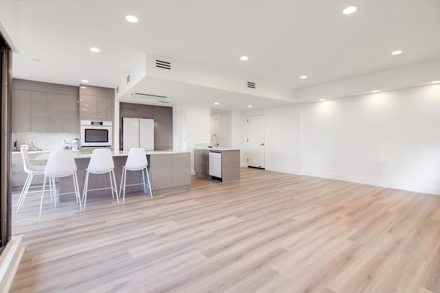 kitchen featuring a breakfast bar area, oven, gray cabinetry, a kitchen island, and light wood-type flooring