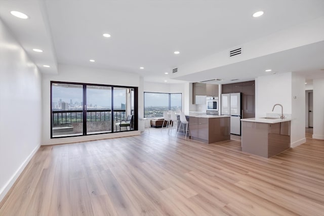 kitchen with white refrigerator, sink, an island with sink, oven, and light hardwood / wood-style flooring