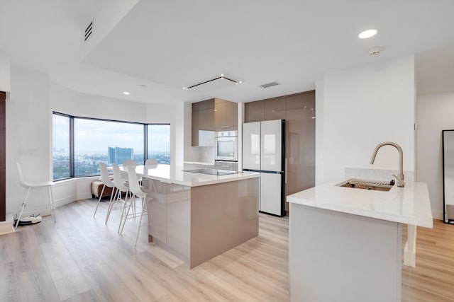 kitchen featuring sink, a breakfast bar area, gray cabinets, white fridge, and light hardwood / wood-style flooring