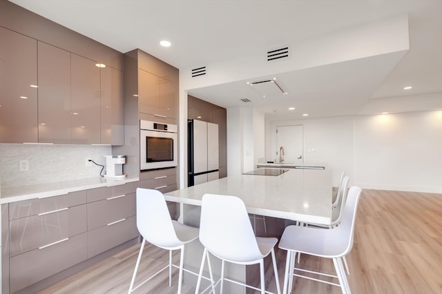 kitchen featuring backsplash, gray cabinets, a breakfast bar, white appliances, and light hardwood / wood-style flooring