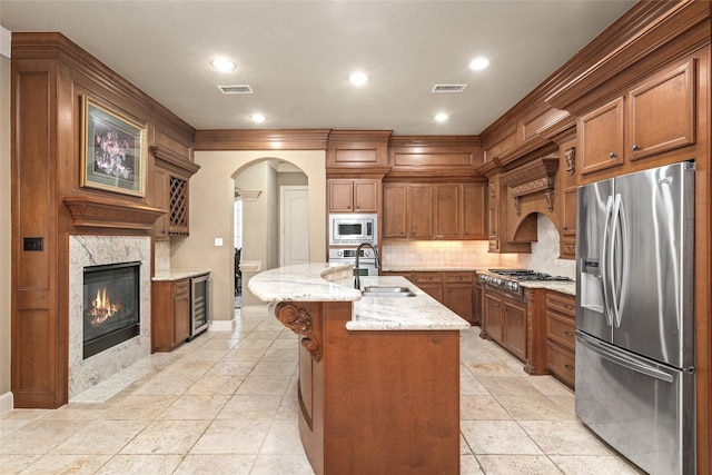 kitchen featuring sink, beverage cooler, a kitchen island with sink, a fireplace, and appliances with stainless steel finishes