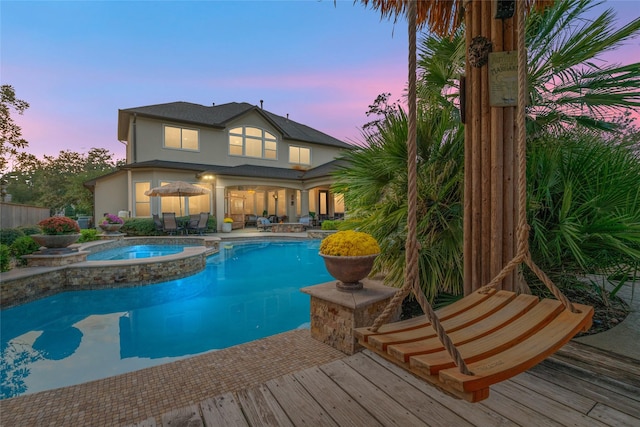 pool at dusk with a deck and an in ground hot tub