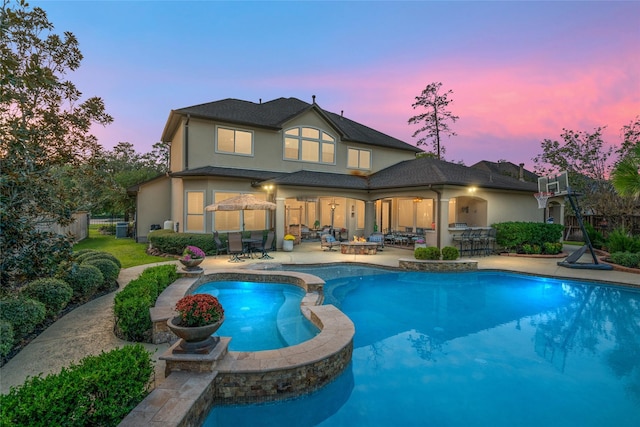 back house at dusk with an outdoor hangout area, a patio area, and a pool with hot tub