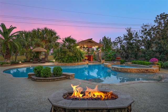 pool at dusk with a gazebo, a patio area, an in ground hot tub, and an outdoor fire pit