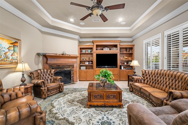 tiled living room with a fireplace, a tray ceiling, ceiling fan, and crown molding