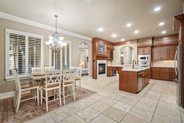 kitchen with hanging light fixtures, stainless steel appliances, crown molding, decorative backsplash, and a center island with sink