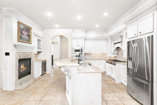 kitchen with a center island with sink, white cabinets, sink, stainless steel appliances, and beverage cooler