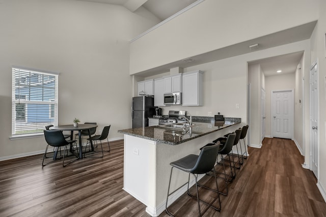 kitchen with sink, white cabinetry, stainless steel appliances, a kitchen bar, and kitchen peninsula