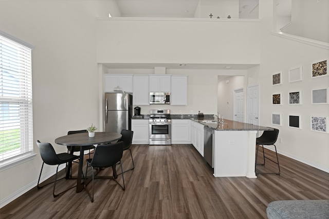 kitchen with sink, a breakfast bar area, appliances with stainless steel finishes, white cabinetry, and dark stone countertops