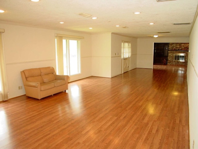 unfurnished living room featuring hardwood / wood-style flooring, a brick fireplace, a textured ceiling, and crown molding